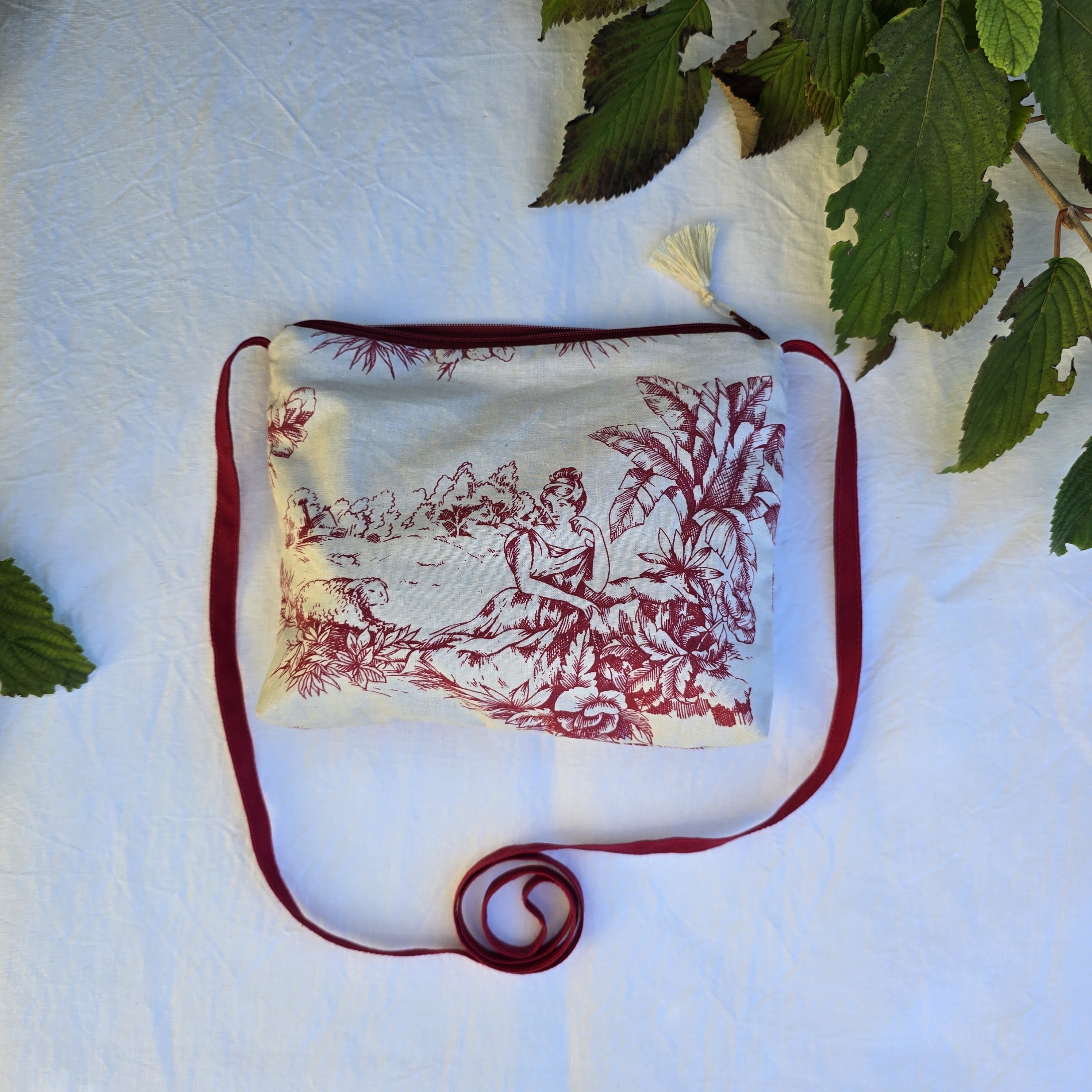 Pochette avec bandouli&egrave;re en tissu toile de Jouy bordeaux et &eacute;cru agr&eacute;ment&eacute;e d'un pompon