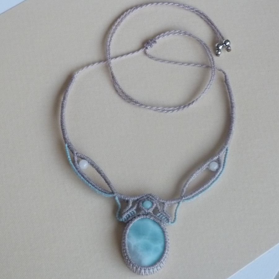 Ketting in taupegrijs/roestblauw micro-macramé met een natuurlijke edelsteen in zachte tinten wit en lichtblauw als middelpunt.