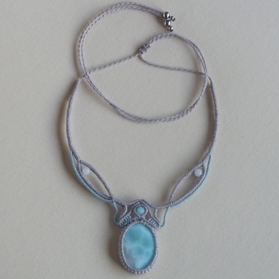 Ketting in taupegrijs/roestblauw micro-macramé met een natuurlijke edelsteen in zachte tinten wit en lichtblauw als middelpunt.