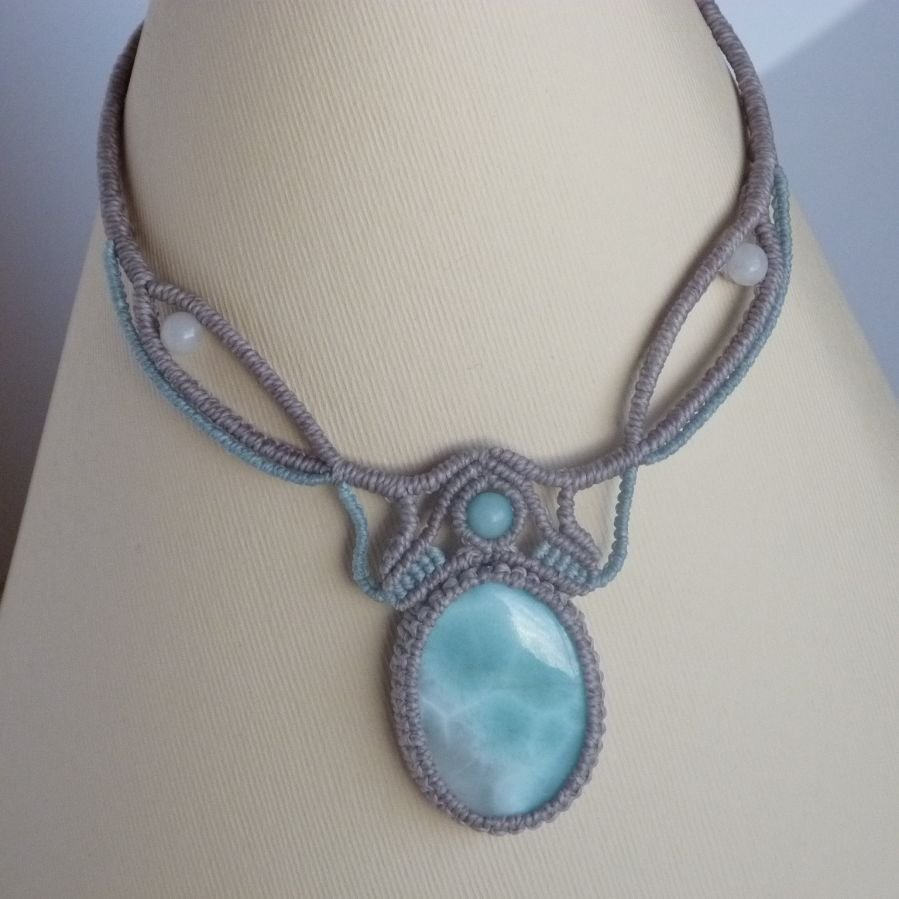 Ketting in taupegrijs/roestblauw micro-macramé met een natuurlijke edelsteen in zachte tinten wit en lichtblauw als middelpunt.
