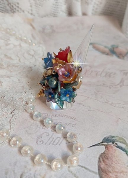 Bague Bel Air mont&eacute;e avec des fleurs lucites peintes &agrave; la main aux couleurs : Bleu, Rose, Rouge, Argent, Blanc avec feuilles ondul&eacute;es Vert Cuivr&eacute; &agrave; laquelle s&rsquo;ajoute perles Dor&eacute;es en Verre