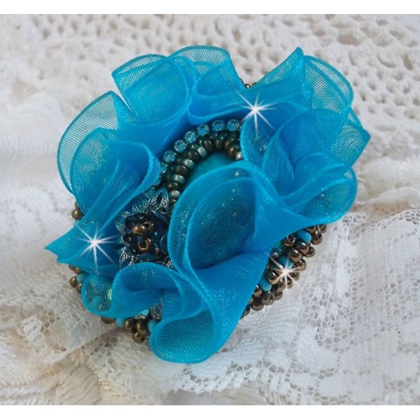 Ilycia Charmante ring geborduurd met een facet geslepen turquoise blauwe hars cabochon en een organza lint