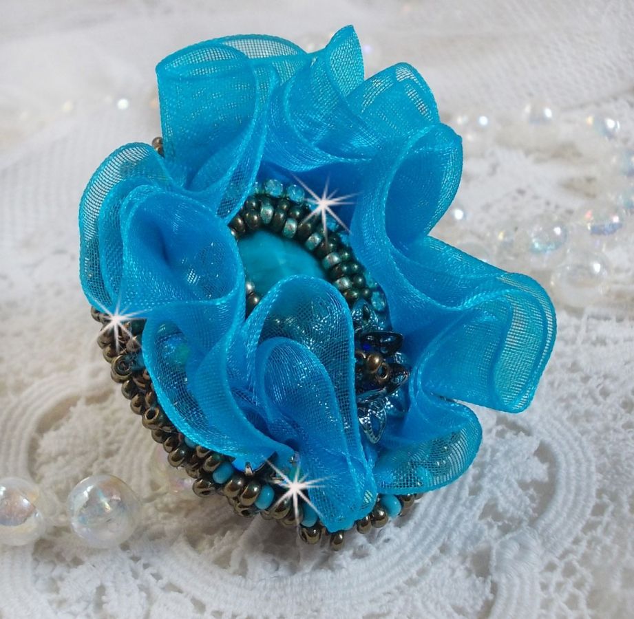 Ilycia Charmante ring geborduurd met een facet geslepen turquoise blauwe hars cabochon en een organza lint