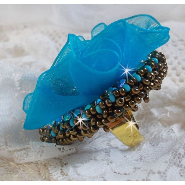 Ilycia Charmante ring geborduurd met een facet geslepen turquoise blauwe hars cabochon en een organza lint