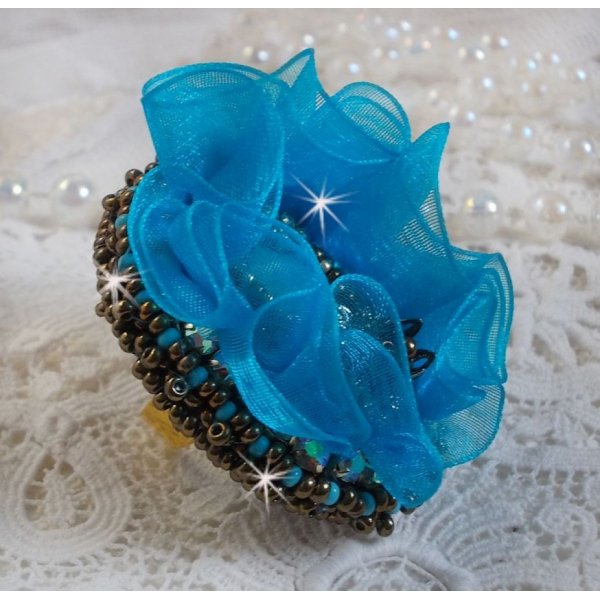 Ilycia Charmante ring geborduurd met een facet geslepen turquoise blauwe hars cabochon en een organza lint
