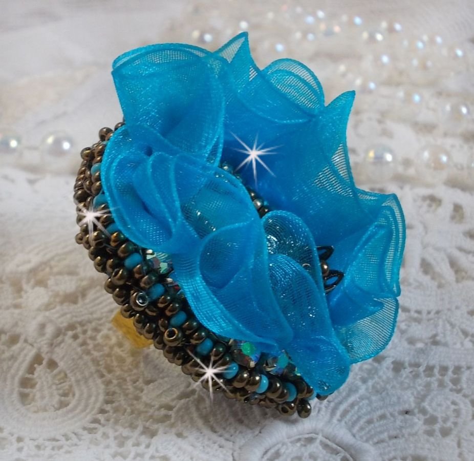 Ilycia Charmante ring geborduurd met een facet geslepen turquoise blauwe hars cabochon en een organza lint