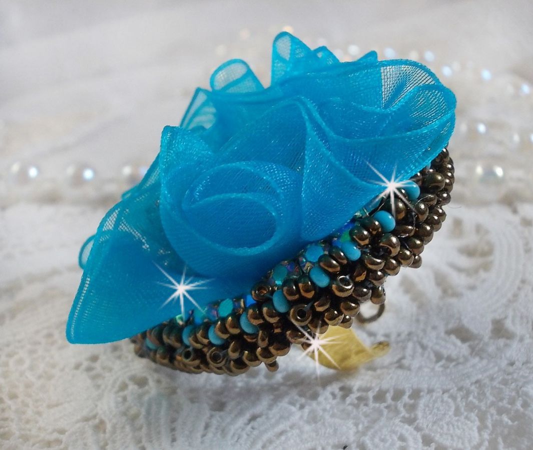 Ilycia Charmante ring geborduurd met een facet geslepen turquoise blauwe hars cabochon en een organza lint