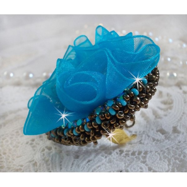 Ilycia Charmante ring geborduurd met een facet geslepen turquoise blauwe hars cabochon en een organza lint