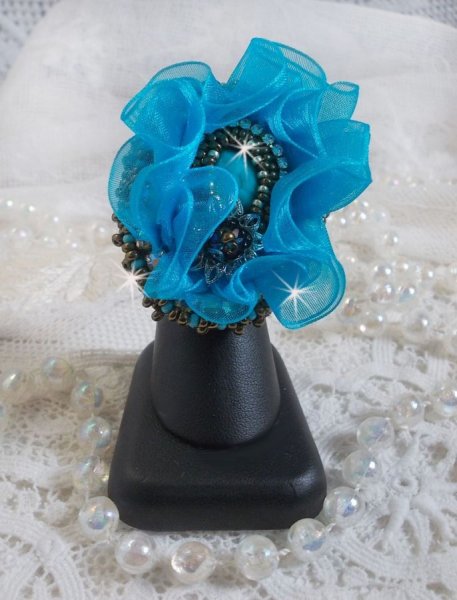 Ilycia Charmante ring geborduurd met een facet geslepen turquoise blauwe hars cabochon en een organza lint