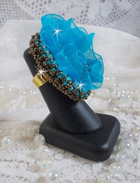 Ilycia Charmante ring geborduurd met een facet geslepen turquoise blauwe hars cabochon en een organza lint