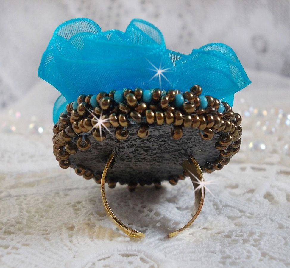 Ilycia Charmante ring geborduurd met een facet geslepen turquoise blauwe hars cabochon en een organza lint