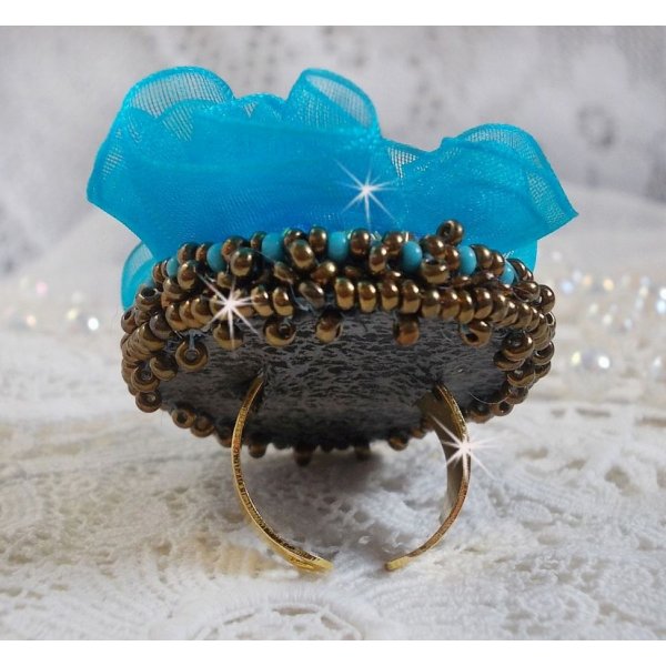 Ilycia Charmante ring geborduurd met een facet geslepen turquoise blauwe hars cabochon en een organza lint