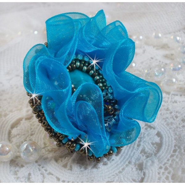 Ilycia Charmante ring geborduurd met een facet geslepen turquoise blauwe hars cabochon en een organza lint