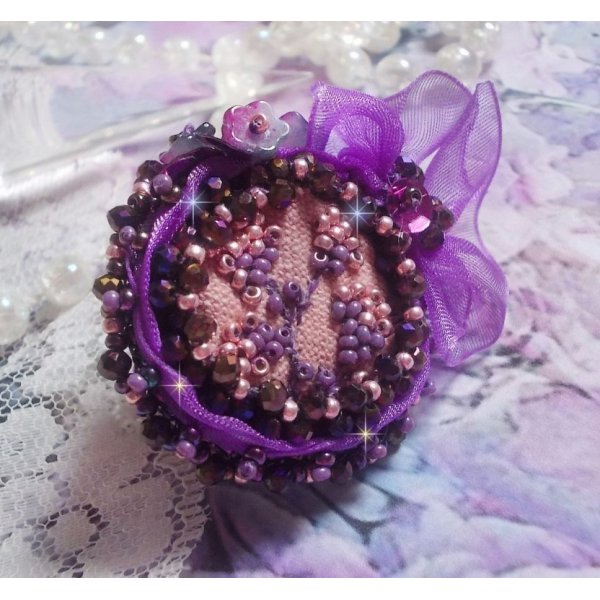 Romantische damesring geborduurd op een roze linnen stof met roze, iris, paars en perzikkleurige rocailles. 