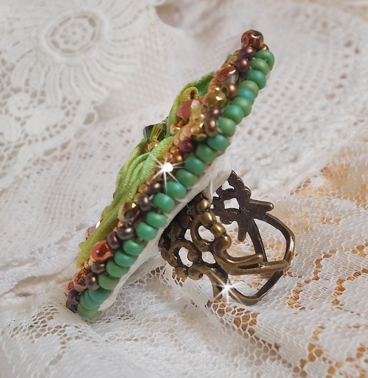 Venetiaanse maanring geborduurd met kameleonkleurig zijden lint, Swarovski kristallen, diverse parels en rocailles.