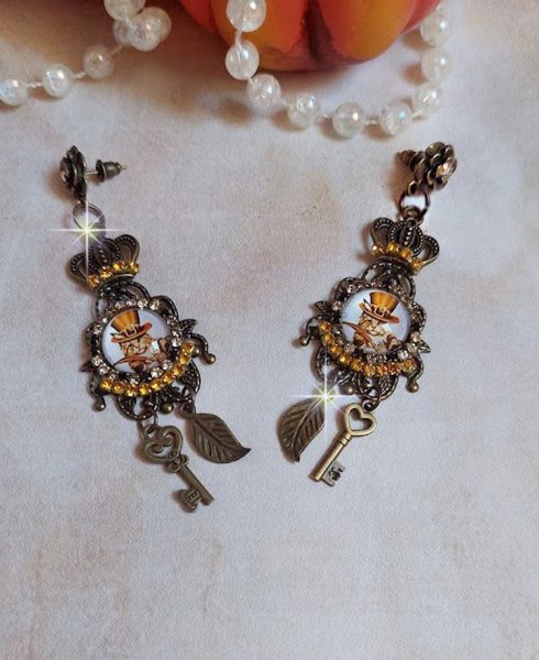 BO Chatibo Steampunk mont&eacute;es avec cabochons ronds en verre repr&eacute;sentant un chat chapeaut&eacute; Haute de Forme Orange. Strass&eacute;es avec une couronne, breloques cl&eacute;s et feuilles. Mont&eacute;es sur clips Bronze