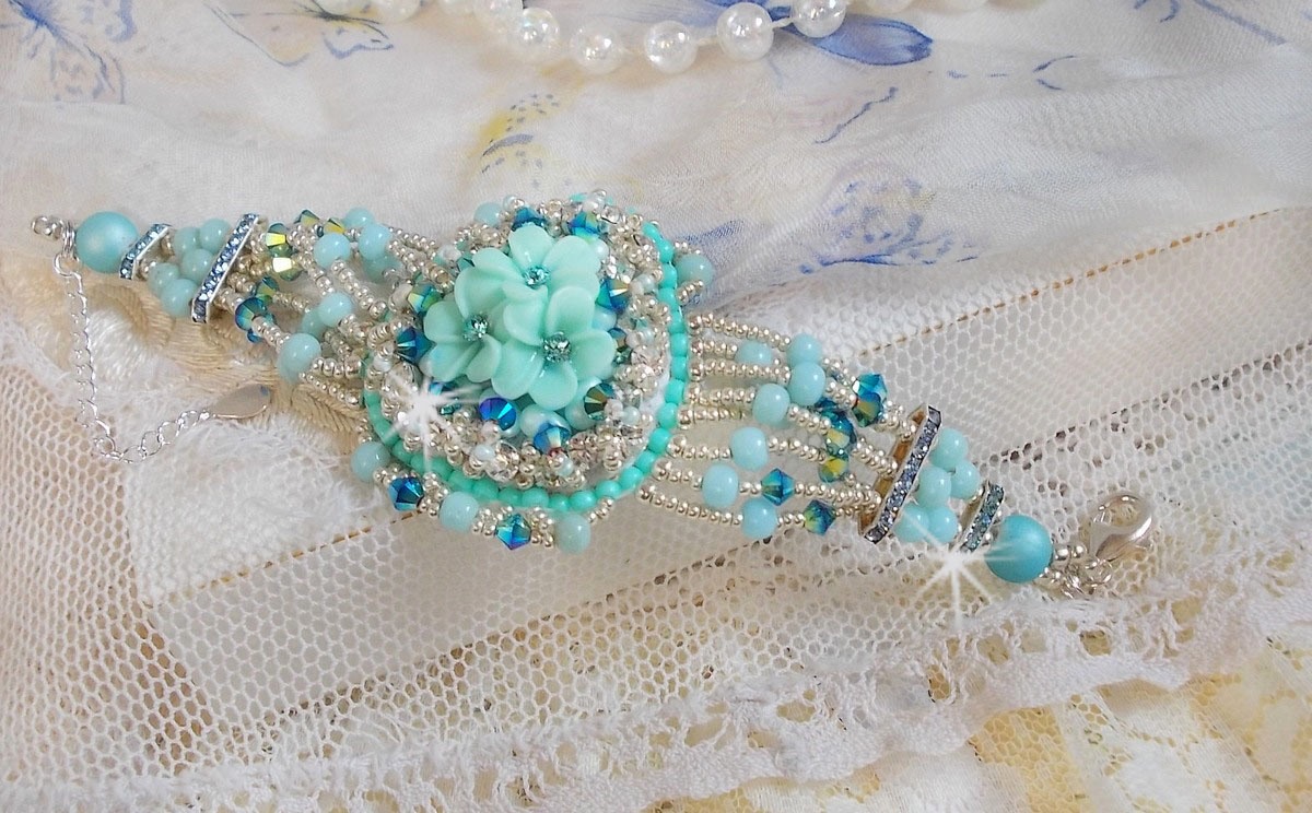 Bracelet Blue Flowers Haute-Couture brodé avec des Cristaux de Swarovski, un cabochon en résine, des perles rondes en satin, des rocailles avec une chaînette et un fermoir en Argent 925/1000