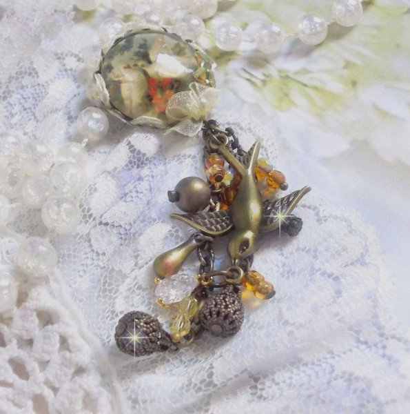 Broche Colombes aux plumages blancs avec des breloques filigran&eacute;es gouttes et lisses, perles rondes et n&oelig;ud en cristal, ruban organza cr&egrave;me, pendentif plaqu&eacute; or avec un zircon sur une broche en m&eacute;tal