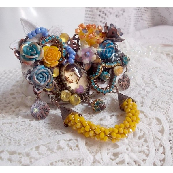 Broche Eclats P&eacute;tillants d&rsquo;inspiration Baroque, orn&eacute;e de fleurs en r&eacute;sine autour d&rsquo;un cabochon strass&eacute;s et perl&eacute;s sur estampes, cristaux, breloques, perle cloisonn&eacute;e, perles jaunes en verre et roses. 