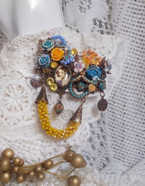 Broche Eclats P&eacute;tillants d&rsquo;inspiration Baroque, orn&eacute;e de fleurs en r&eacute;sine autour d&rsquo;un cabochon strass&eacute;s et perl&eacute;s sur estampes, cristaux, breloques, perle cloisonn&eacute;e, perles jaunes en verre et roses. 