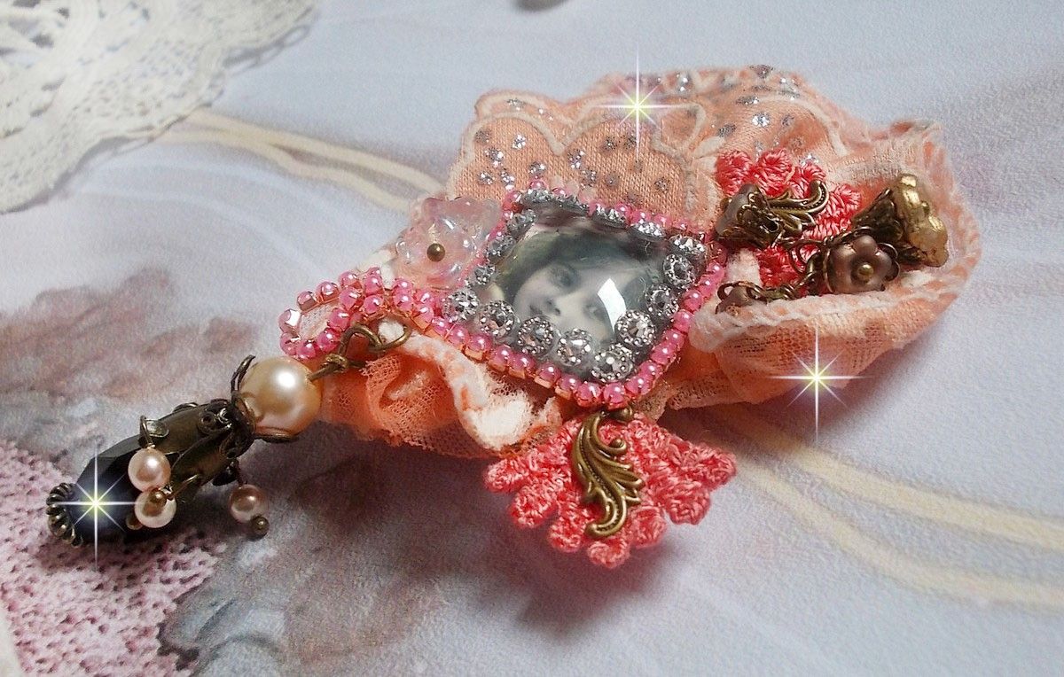 Rustieke rozenbroche gemaakt met een cabochon die een lachend meisje voorstelt, oranje strass- en rozenkant, kristallen, glazen kralen en diverse accessoires.