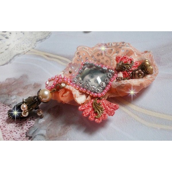Rustieke rozenbroche gemaakt met een cabochon die een lachend meisje voorstelt, oranje strass- en rozenkant, kristallen, glazen kralen en diverse accessoires.