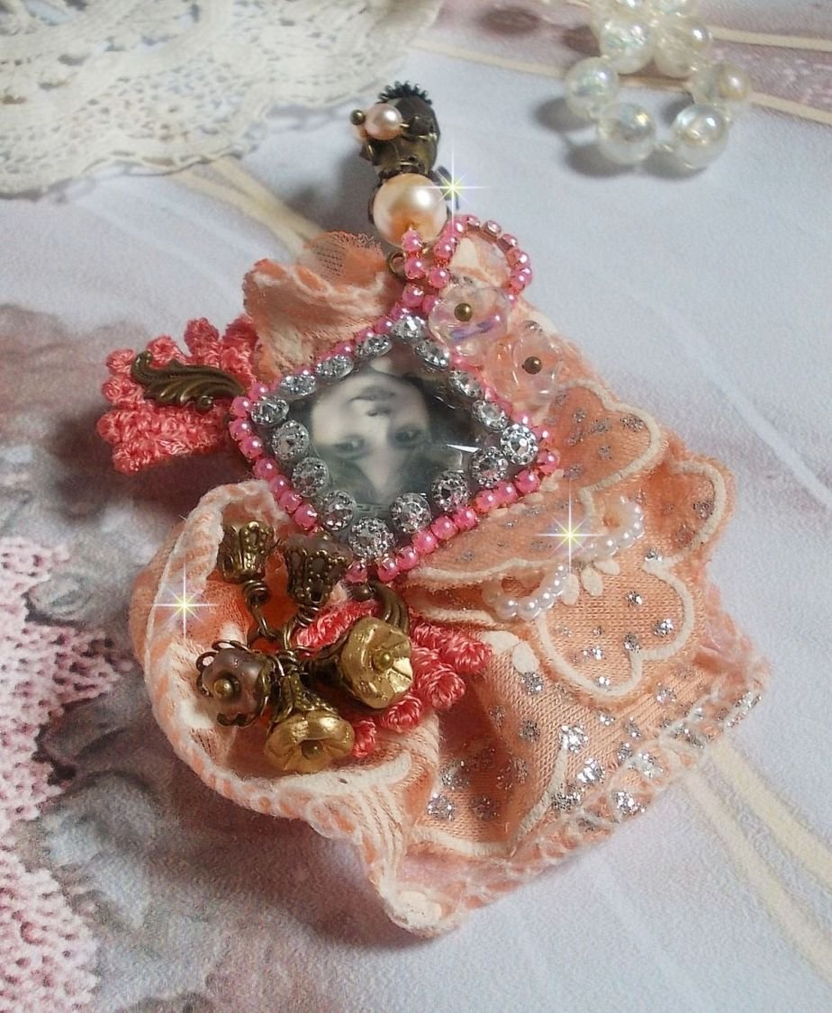 Rustieke rozenbroche gemaakt met een cabochon die een lachend meisje voorstelt, oranje strass- en rozenkant, kristallen, glazen kralen en diverse accessoires.