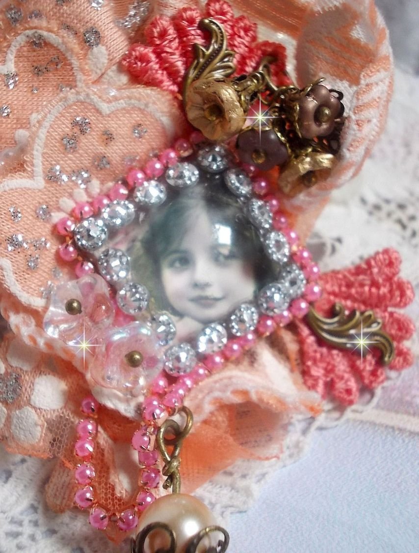 Rustieke rozenbroche gemaakt met een cabochon die een lachend meisje voorstelt, oranje strass- en rozenkant, kristallen, glazen kralen en diverse accessoires.