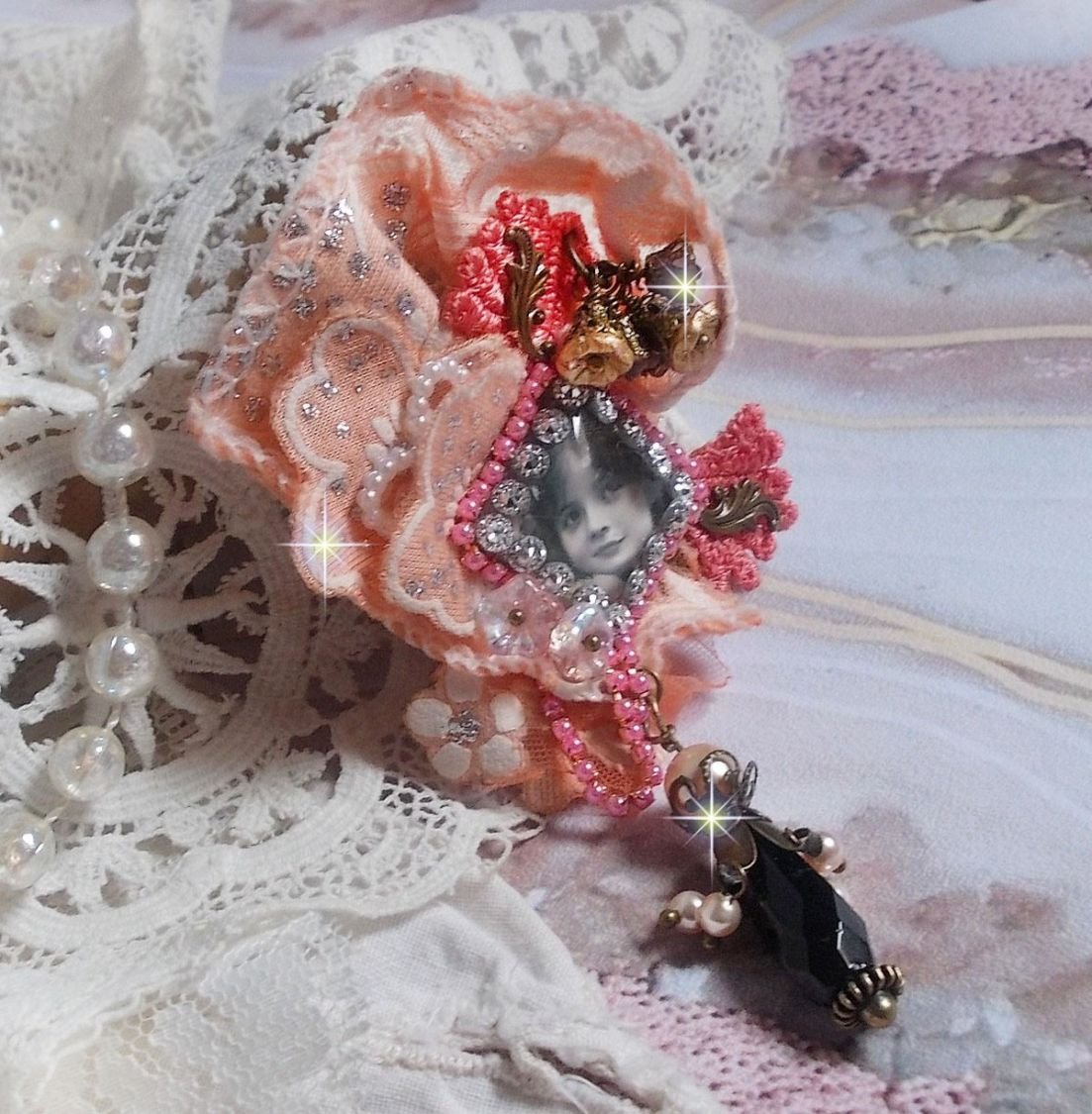 Rustieke rozenbroche gemaakt met een cabochon die een lachend meisje voorstelt, oranje strass- en rozenkant, kristallen, glazen kralen en diverse accessoires.