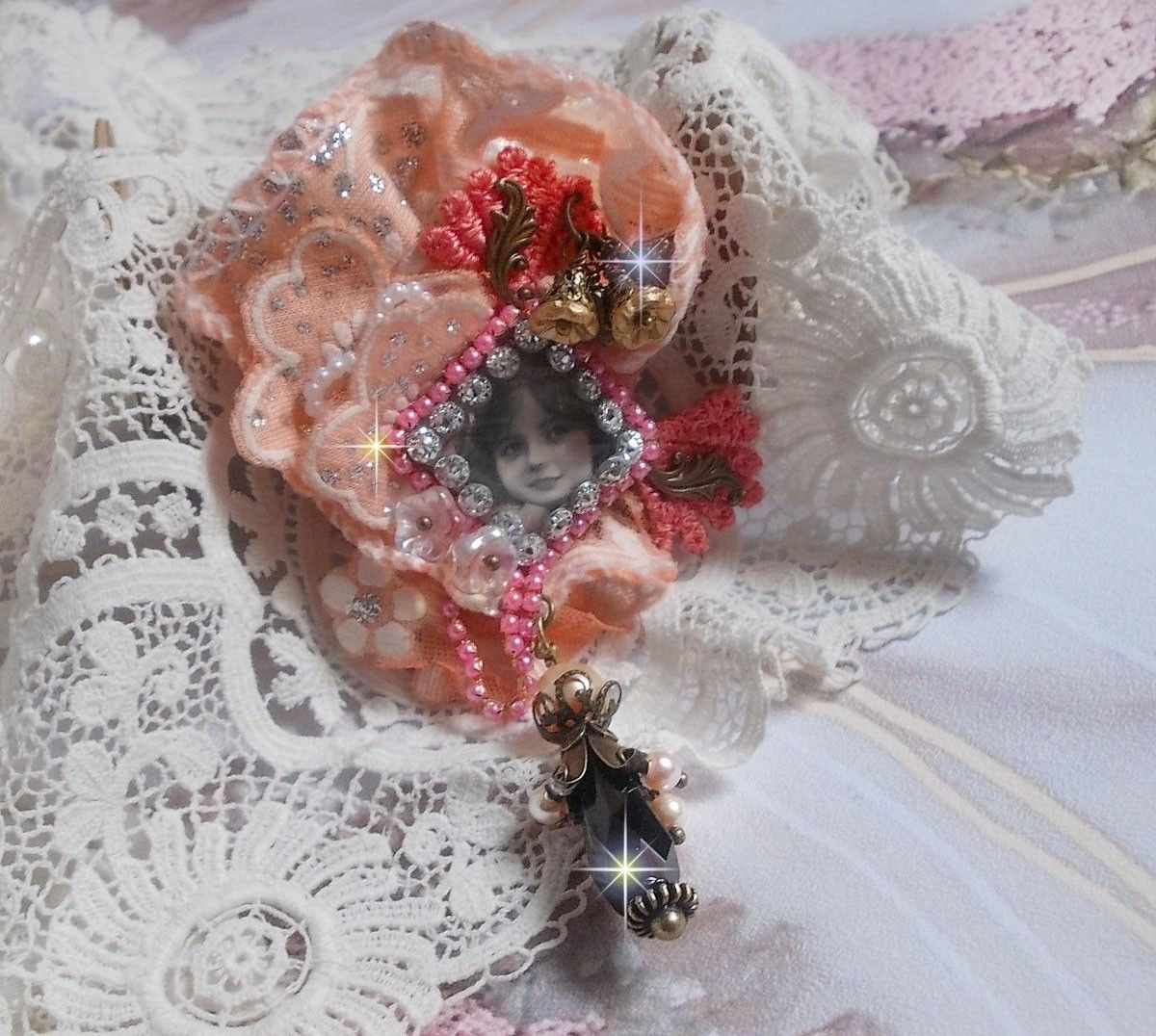 Rustieke rozenbroche gemaakt met een cabochon die een lachend meisje voorstelt, oranje strass- en rozenkant, kristallen, glazen kralen en diverse accessoires.