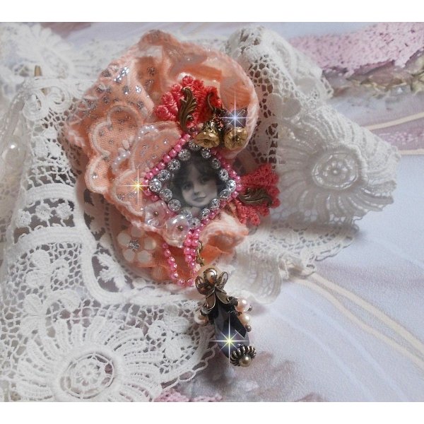 Rustieke rozenbroche gemaakt met een cabochon die een lachend meisje voorstelt, oranje strass- en rozenkant, kristallen, glazen kralen en diverse accessoires.