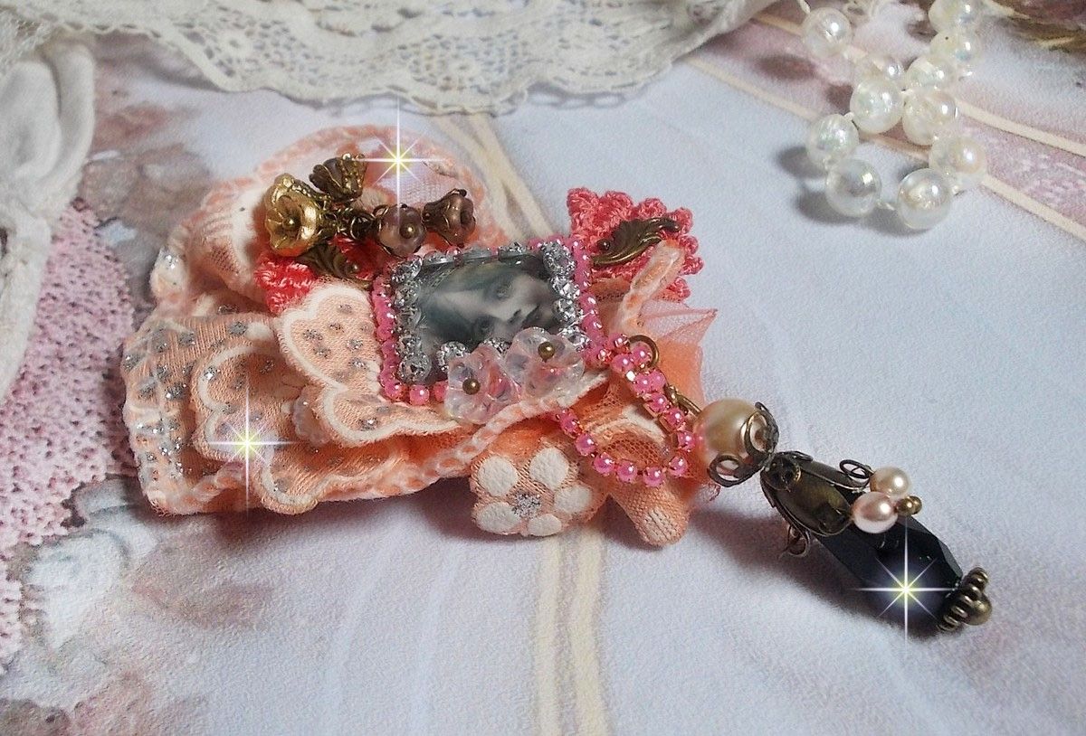 Rustieke rozenbroche gemaakt met een cabochon die een lachend meisje voorstelt, oranje strass- en rozenkant, kristallen, glazen kralen en diverse accessoires.