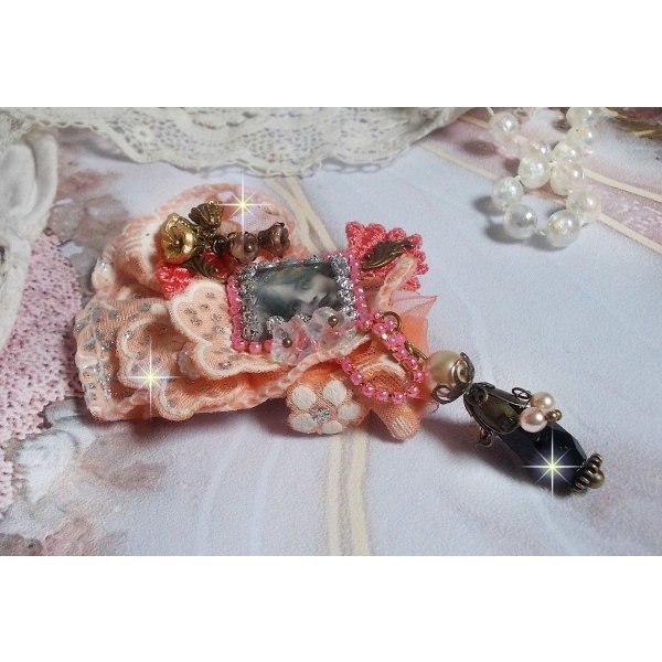 Rustieke rozenbroche gemaakt met een cabochon die een lachend meisje voorstelt, oranje strass- en rozenkant, kristallen, glazen kralen en diverse accessoires.