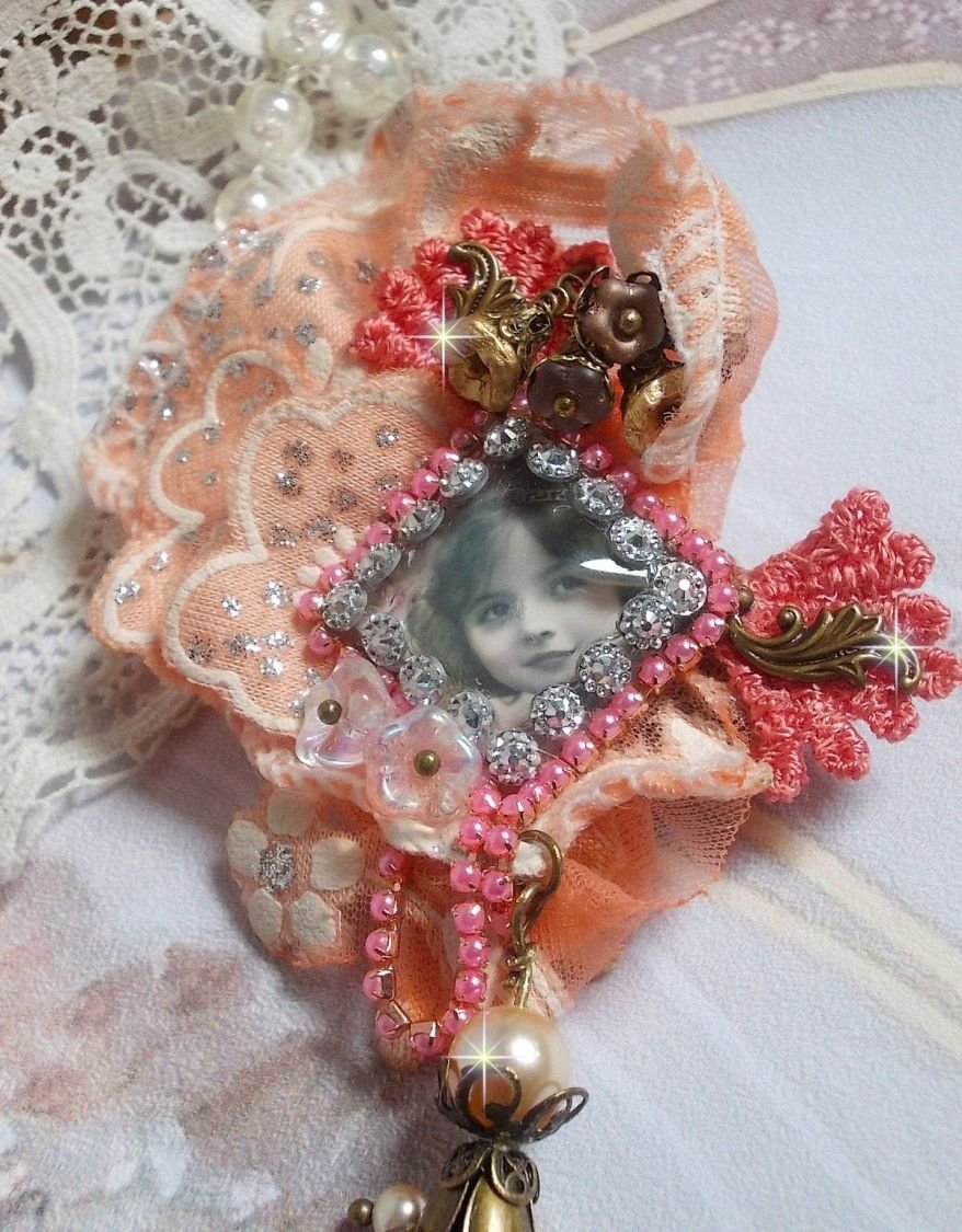 Rustieke rozenbroche gemaakt met een cabochon die een lachend meisje voorstelt, oranje strass- en rozenkant, kristallen, glazen kralen en diverse accessoires.