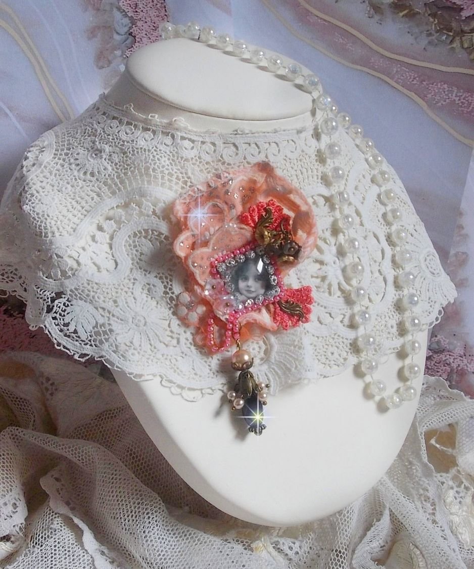 Rustieke rozenbroche gemaakt met een cabochon die een lachend meisje voorstelt, oranje strass- en rozenkant, kristallen, glazen kralen en diverse accessoires.