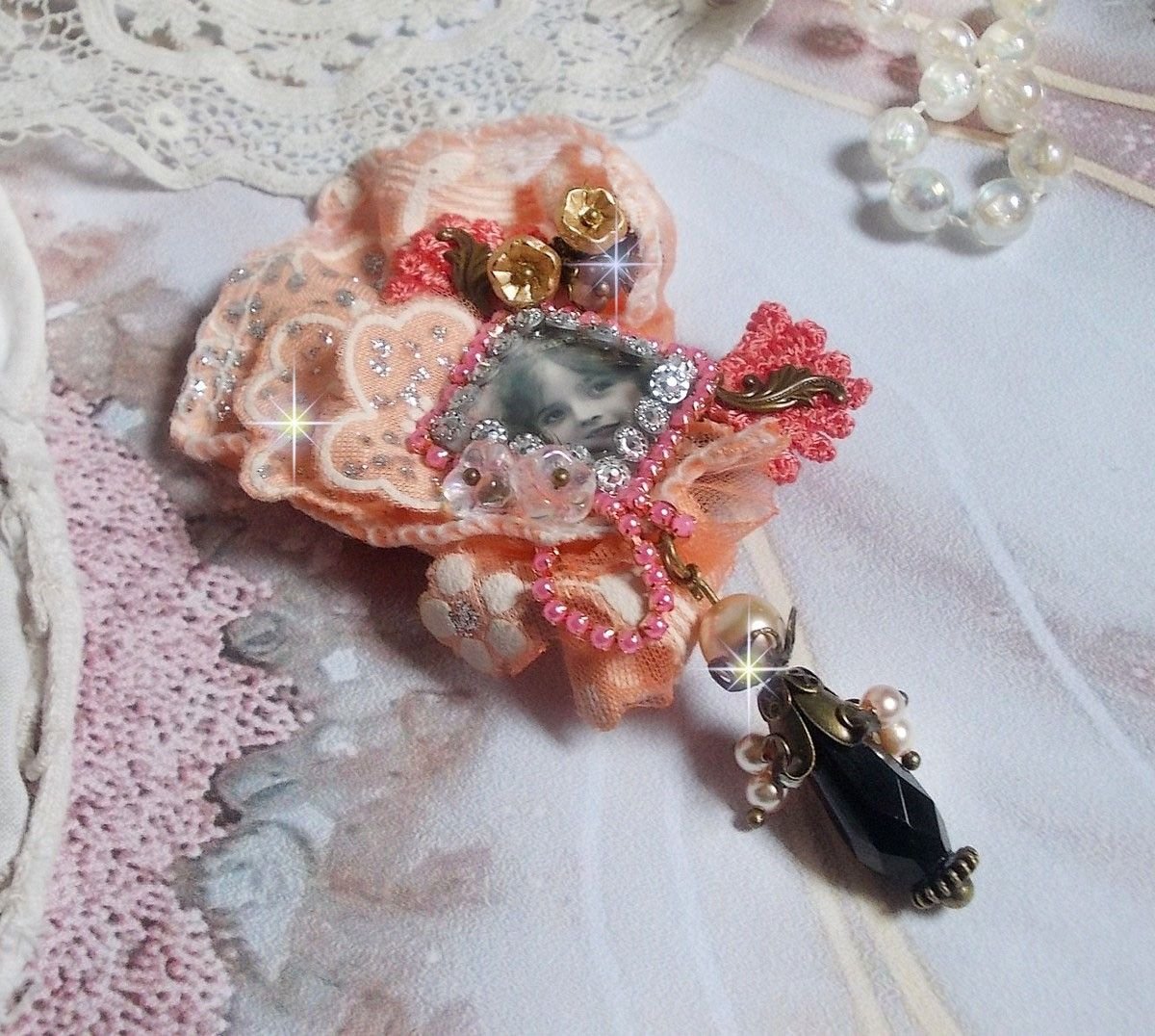 Rustieke rozenbroche gemaakt met een cabochon die een lachend meisje voorstelt, oranje strass- en rozenkant, kristallen, glazen kralen en diverse accessoires.