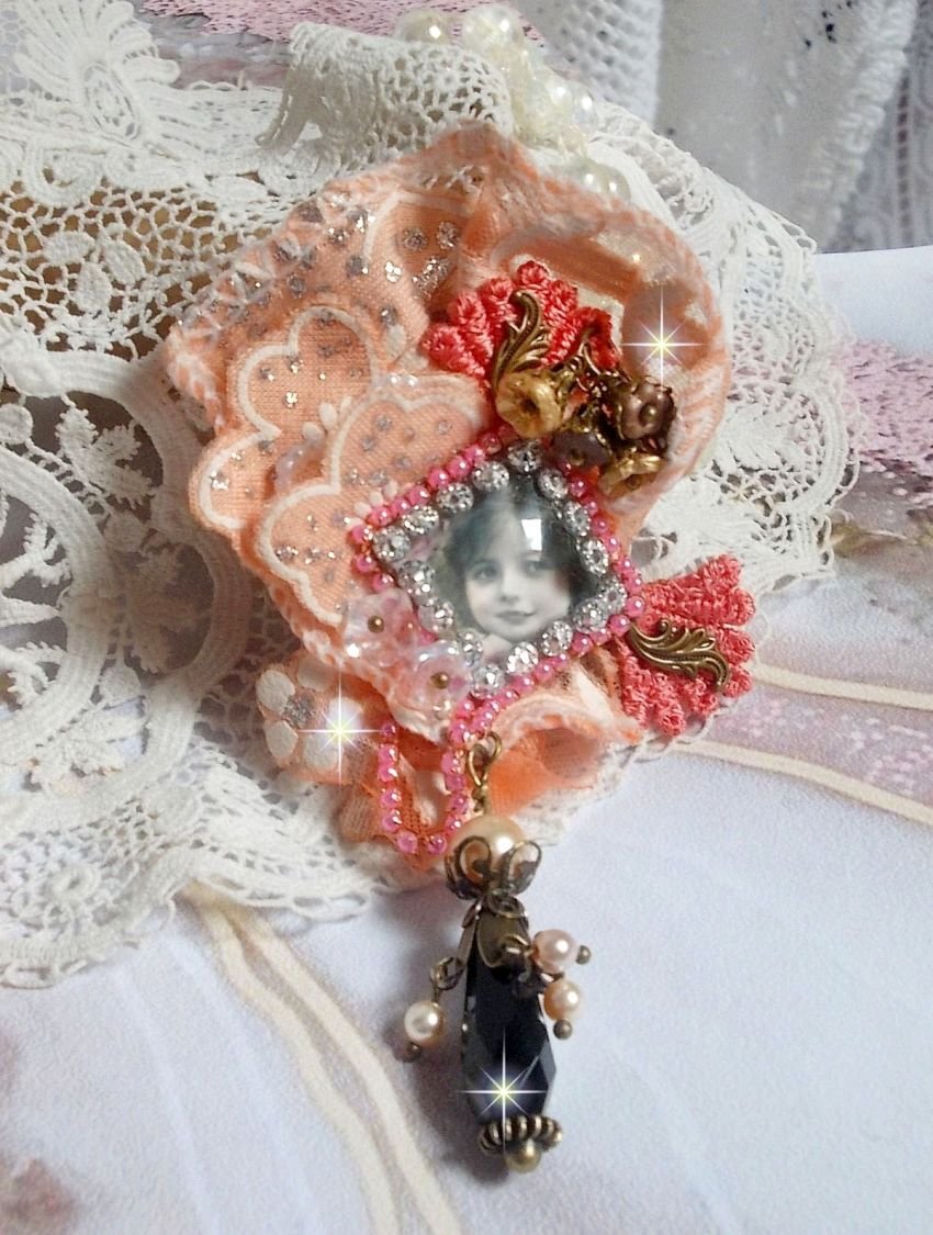 Rustieke rozenbroche gemaakt met een cabochon die een lachend meisje voorstelt, oranje strass- en rozenkant, kristallen, glazen kralen en diverse accessoires.