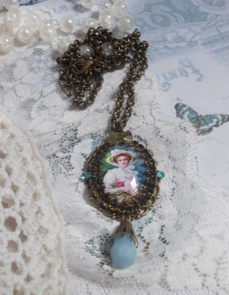 Pendentif Douce Dame cr&eacute;&eacute; avec un cabochon repr&eacute;sentant une femme au chapeau blanc orn&eacute; de cristaux, des accessoires de couleur Bronze et un jade teint&eacute; bleu 