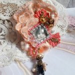 Rustieke rozenbroche gemaakt met een cabochon die een lachend meisje voorstelt, oranje strass- en rozenkant, kristallen, glazen kralen en diverse accessoires.
